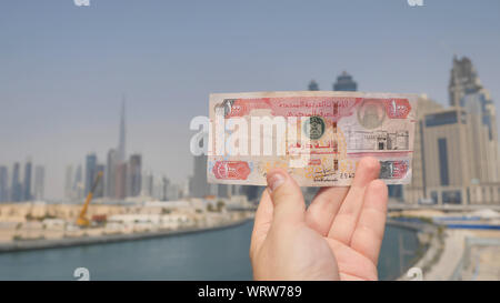 Un uomo detiene una banconota di 100 dirhams nelle mani della città di Dubai. Il denaro degli Emirati Arabi Uniti. Foto Stock