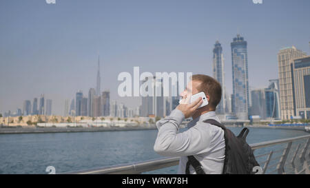 Giovane uomo che parla al telefono sullo sfondo del panorama di Dubai. Canto close-up. Foto Stock
