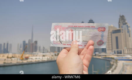 Un uomo detiene una banconota di 100 dirhams nelle mani della città di Dubai. Il denaro degli Emirati Arabi Uniti. Foto Stock
