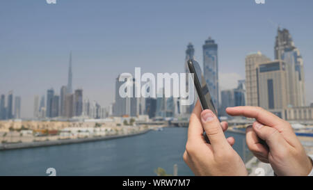 Un uomo stampa un messaggio sul telefono cellulare con lo sfondo del panorama di Dubai. Canto close-up. Foto Stock