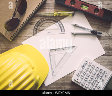 La documentazione con la scrittura di materiali di costruzione, casco, occhiali da sole, blocco note, calcolatrice e di strumenti di costruzione di architettura sul tavolo di legno Foto Stock