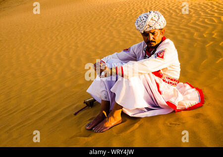 Jaisalmer, Rajasthan, India - aprile 18th, 2018: Villaggio Indiano uomo seduto nel deserto di dune di sabbia che indossa etnici abiti tradizionali, la vita del villaggio concep Foto Stock