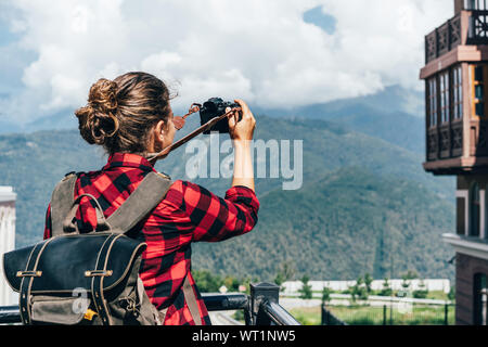 Donna con uno zaino prende le immagini su una fotocamera di montagna. Foto Stock