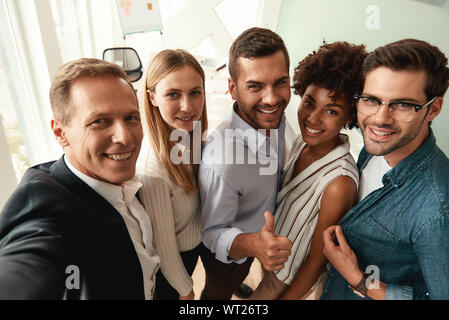 Il gruppo di allegro colleghi tenendo selfie e gesticolando permanente, mentre nell'ufficio moderno. Concetto di fotografia. Lavoro di squadra Foto Stock