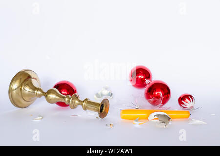 Vista frontale di caduta e frantumato rosso e argento baubles di Natale e un bronzo candelabro con una candela di colore giallo su sfondo bianco Foto Stock