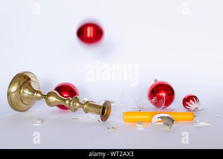 Vista frontale di caduta e frantumato rosso e argento baubles di Natale e un bronzo candelabro con una candela di colore giallo su sfondo bianco Foto Stock