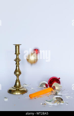 Vista frontale di caduta e frantumato rosso e argento baubles di Natale e un bronzo candelabro con una candela di colore giallo su sfondo bianco Foto Stock