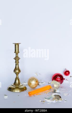 Vista frontale di caduta e frantumato rosso e argento baubles di Natale e un bronzo candelabro con una candela di colore giallo su sfondo bianco Foto Stock