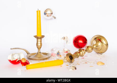 Vista frontale di caduta e frantumato rosso e argento baubles di Natale e due di bronzo portacandele con una candela di colore giallo su sfondo bianco Foto Stock