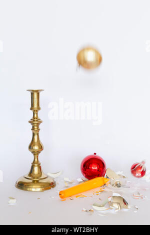 Vista frontale di caduta e frantumato rosso e argento baubles di Natale e un bronzo candelabro con una candela di colore giallo su sfondo bianco Foto Stock