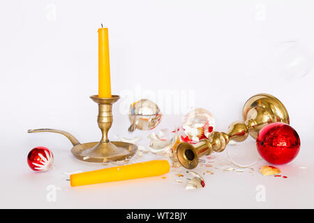 Vista frontale di caduta e frantumato rosso e argento baubles di Natale e due di bronzo portacandele con una candela di colore giallo su sfondo bianco Foto Stock