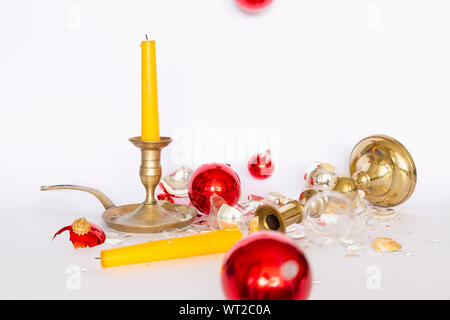 Vista frontale di caduta e frantumato rosso e argento baubles di Natale e due di bronzo portacandele con una candela di colore giallo su sfondo bianco Foto Stock