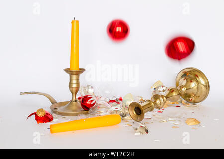 Vista frontale di caduta e frantumato rosso e argento baubles di Natale e due di bronzo portacandele con una candela di colore giallo su sfondo bianco Foto Stock