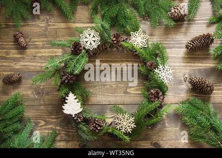 Ghirlanda di Natale con rami di abete e di elementi decorativi di fiocchi di neve sul piano portapaziente in legno di abete e rami di alberi attorno. Lay piatto. Foto Stock