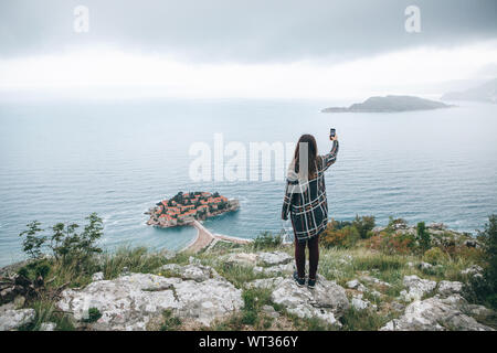 Una ragazza turistico o un blogger prende un selfie o prende le foto o i video di una bella vista in Montenegro. Foto Stock