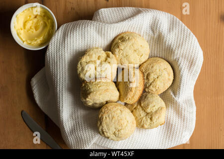 Focaccine - Biscotti fatti con il latticello ricetta nella ciotola con il bianco canovaccio, il burro e il coltello sul tavolo di legno - vista superiore Foto Stock