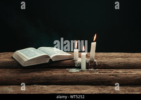 Bellissima Bibbia aperta e bruciate candele su una vecchia quercia tavolo in legno. Sfondo di fumo. Foto Stock