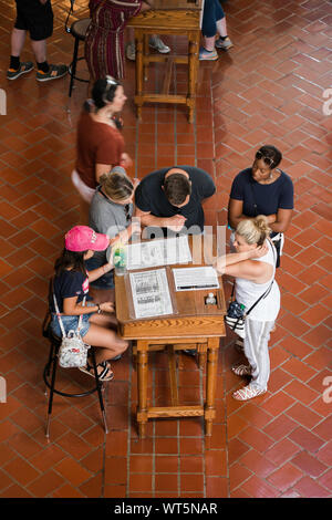 Sala del registro di Ellis Island, vista di turisti in piedi intorno a un funzionario dell'ufficio immigrazione la scrivania nella sala del Registro di sistema, Ellis Island, New York City, Stati Uniti d'America Foto Stock