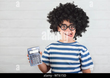Funny bambino con la calcolatrice indossando occhiali nerd su Sfondo mattone Foto Stock