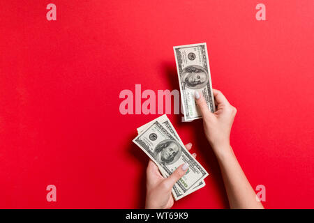 Mano femminile dando un centinaio di dollari di banconote su sfondo colorato. Vista superiore del concetto di ricchezza con spazio vuoto per il tuo design. Foto Stock