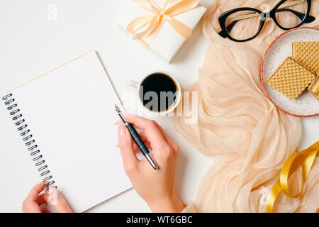 Donna home office desk. Area di lavoro con mani femminili messaggio di scrittura nel notebook di carta e femminile golden accessori moda su sfondo bianco. G Foto Stock