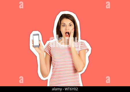 Ritratto di un scioccato la ragazza con una bocca aperta che mostra un fustellato telefono cellulare schermo. ragazza emotiva rivista stile collage alla moda e colore di sfondo. Foto Stock