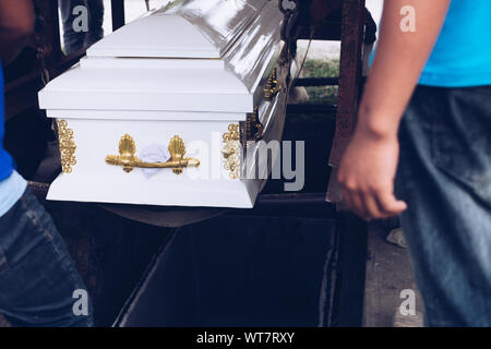 Pallbearers sorvegliare attentamente il processo di abbassamento del scrigno di massa per il defunto al suo ultimo luogo di riposo durante il servizio di sepoltura Foto Stock