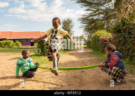 Imani Junior Academy, Nanyuki, contea di Laikipia, Kenya - Giugno 13th, 2019: Candida fotografia della scuola di giovani bambini che salta con una corda improvvisata o Foto Stock