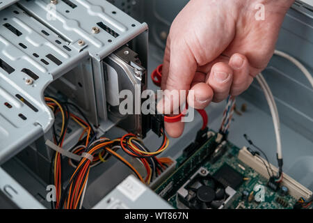 Mano di uomo di tamponamento (SATA seriale AT Attachment, Serial ATA) il cavo di dati nel disco rigido periferica. Calcolatore di interfaccia bus per collegare dispositivi di archiviazione di massa, Foto Stock