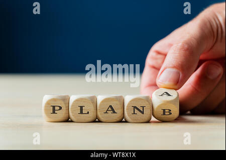 Il piano A o B segno scritto su plinti in legno con maschio girando a mano l'ultimo dado. Su sfondo blu scuro. Foto Stock