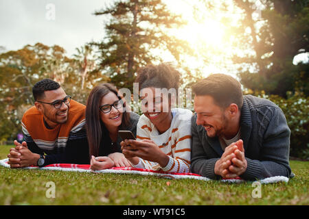 Sorridente americano africano donna sdraiata con il suo gruppo multietnico di amici gli sms su un cellulare in un parco - molto felice gruppo di amici Foto Stock