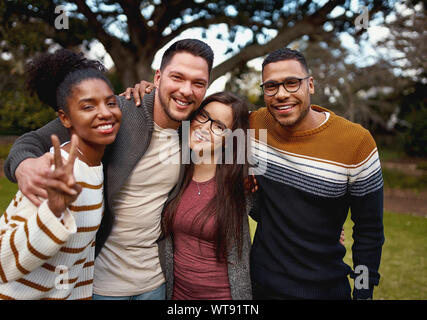 Gruppo di giovani multi razziale americano africano amici in piedi e sorridente insieme nel parco - Vestiti caldi Foto Stock