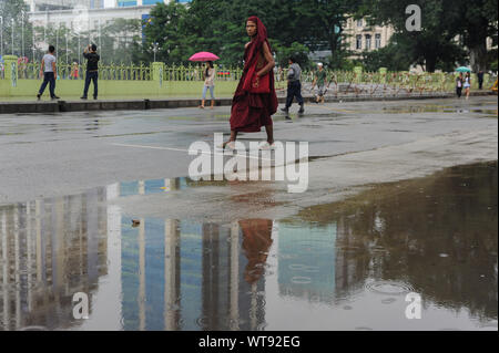 27.09.2013, Yangon, Myanmar, Asia - un monaco buddista passeggiate da una pozzanghera riflettendo edifici durante la stagione delle piogge. Foto Stock