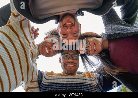 Basso angolo di visualizzazione molto gentile diverse multi-etnico amici formando un cerchio e guardando la telecamera sorridendo - il lavoro di squadra Foto Stock