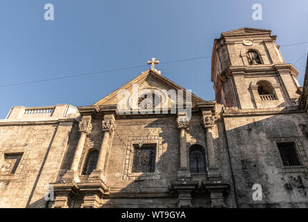 Manila, Filippine - Marzo 5, 2019: San Augustin. Luce della Sera su marrone facciata in pietra e la torre dell orologio sotto il cielo blu. Foto Stock