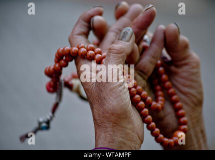 Vecchia donna mani japamala durante il culto Foto Stock