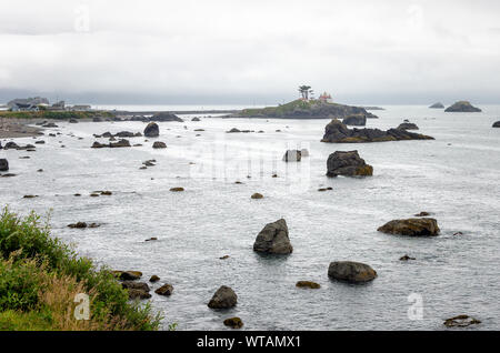 Baia punteggiata di pile di mare e un'isola con un faro lungo la costa della California del Nord in una nebbiosa mattina d'estate Foto Stock