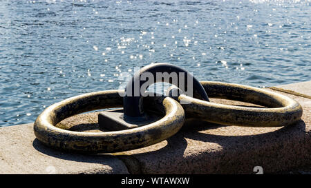 Basso angolo vista di due rusty weathered anelli di ormeggio sul muro di pietra accanto all'acqua Foto Stock