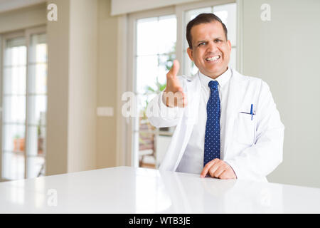 La mezza età medico uomo indossa cappotto medico presso la clinica sorridente cordiale offrendo stretta di mano come saluto e accogliente. Il successo dell'azienda. Foto Stock