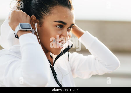 Vista laterale della giovane donna che indossa una felpa con cappuccio. Femmina prendendo una pausa dopo allenamento ascolto di musica Foto Stock