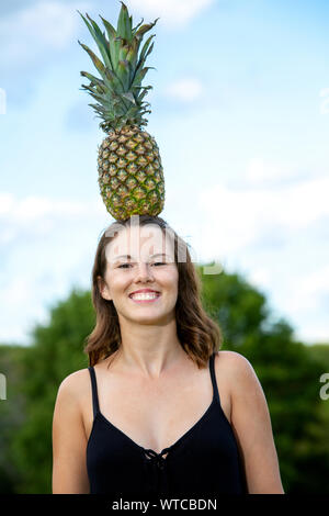 Ritratto di giovane donna bruna equilibratura di un ananas sul suo capo Foto Stock