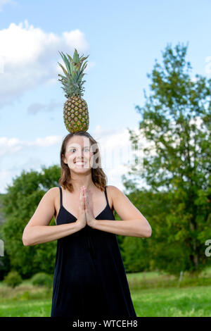 Ritratto di giovane donna bruna equilibratura di un ananas sul suo capo Foto Stock