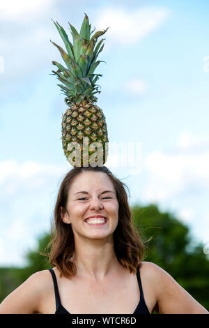 Ritratto di giovane donna bruna equilibratura di un ananas sul suo capo Foto Stock