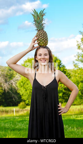 Ritratto di giovane donna bruna equilibratura di un ananas sul suo capo Foto Stock