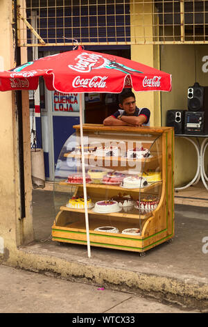 AMBATO, ECUADOR - 12 Maggio 2014: Non identificato un giovane in piedi in un involucro di vetro con diverse torte il 12 maggio 2014 in Ambato, Ecuador. Foto Stock