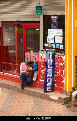 TUNGURAHUA, ECUADOR - 12 Maggio 2014: donna non identificato con il bambino seduto sulle scale all'entrata di un internet cafe in provincia di Tungurahua Foto Stock