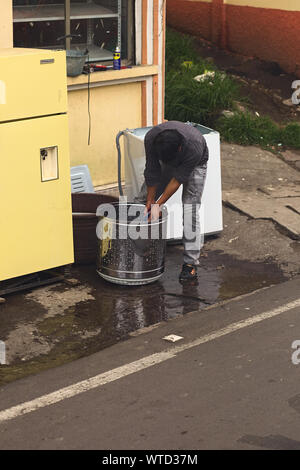 TUNGURAHUA, ECUADOR - 12 Maggio 2014: persona non identificata la pulizia di una vasca di lavaggio con acqua e spazzola sul ciglio della strada nella provincia di Tungurahua, Ecuador Foto Stock