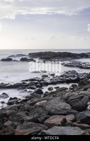 Mesa del mar di ciottoli vulcanici costa, lunga esposizione fotografia, con l'Oceano Atlantico onde, orizzonte con la luce del tramonto, Tacoronte, Tenerife, Canarie Foto Stock