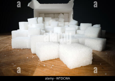 Macro shot di cubetti di zucchero accanto alla scatola di cartone sul tavolo di legno. Cibo malsano dolcificante, dolci cubetti di cristallo Foto Stock
