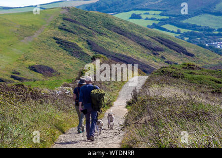 Camminatori con zaino e due cani a piedi su Baggy Point, Croyde, Nr. Braunton, North Devon, Inghilterra, Regno Unito Foto Stock